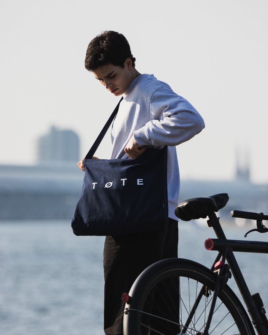 Navy Blue TØTE Bag worn crossbody beside a bicycle